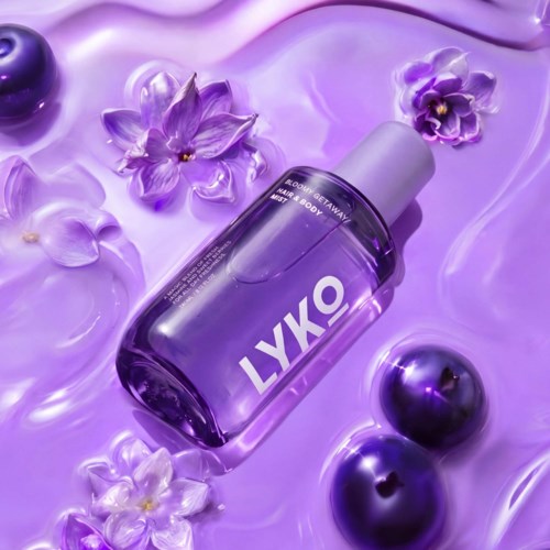 En lila hudvårdsflaska märkt LYKO omgiven av lila blommor och reflekterande lila kulor på en glänsande yta.