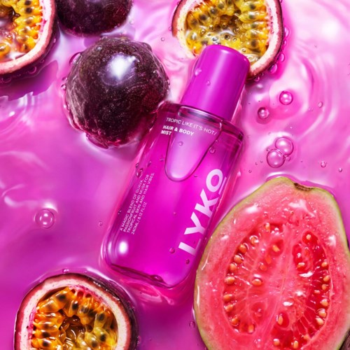 Rosa flaska med Tropic Like Its Hot hår- och kroppsspray omgiven av passionfrukt och vattenmelonskivor på rosa bakgrund.