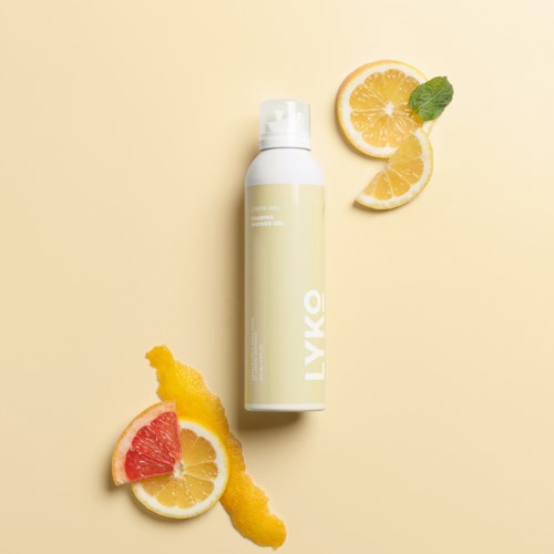 En vit flaska märkt LYKÓ omgiven av citron, grapefrukt och gula citrus-skivor och skal på en ljus bakgrund.