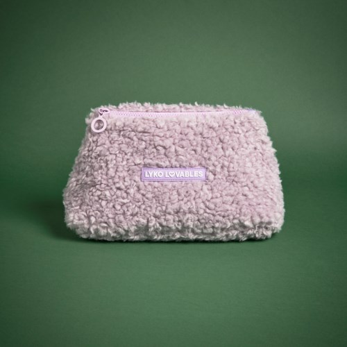 En mjuk, fluffig rosa väska med en lavendelmärke och en dragkedja, placerad mot en grön bakgrund.