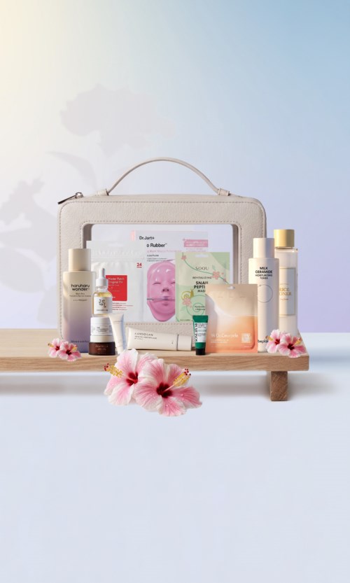 Hudpleieprodukter plassert på en liten trehylle med rosa blomster, reiseveske og en skjerm, mot en pastellbakgrunn.