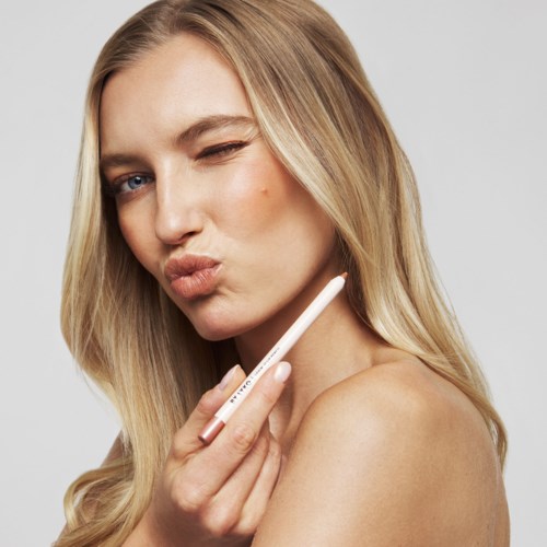 Een vrouw met lang blond haar houdt een make-upkwastje nabij haar gezicht, geeft een speelse kus en knipoogt.