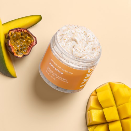 En krukke med mangokroppsskrubb omgitt av skivet banan, pasjonsfrukt og mango biter på en beige bakgrunn.