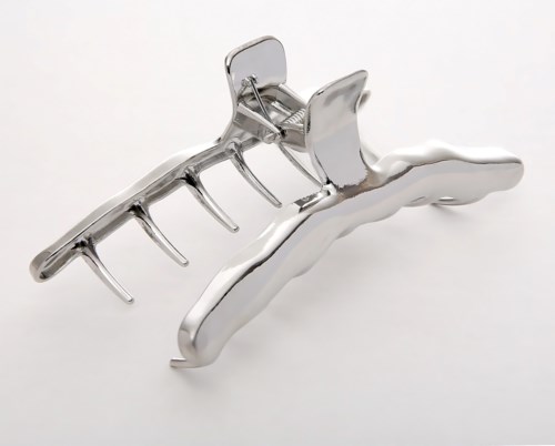 A metallic hair clip with multiple prongs, one side smooth, the other with teeth for grabbing hair.