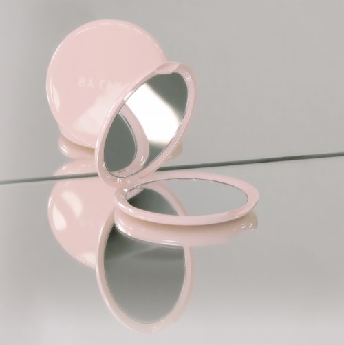En rosa kompakt spegel är öppen, visar sin spegel inuti, på en reflekterande yta.