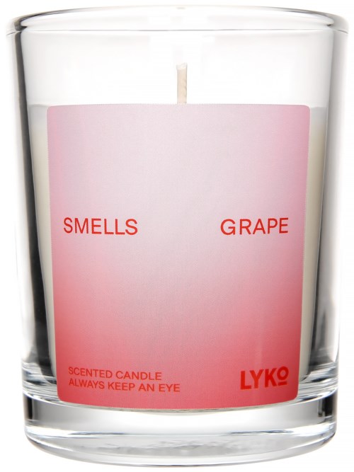 Et duftlys mærket 'Smells Grape' med pink og rød skrift, i et klart glas.