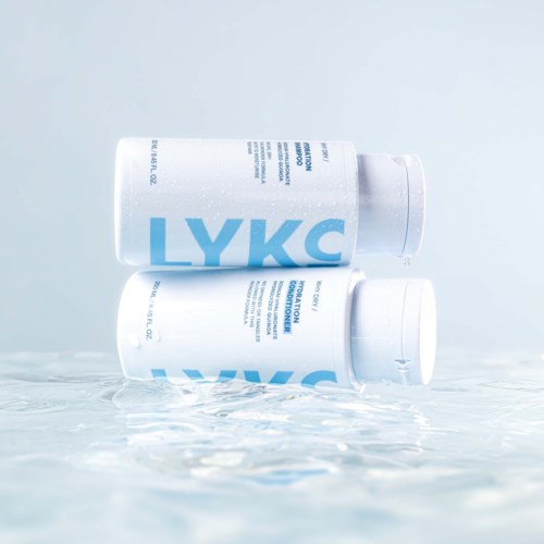 Twee witte flessen met LYKC liggen op een nat oppervlak, water spettert rondom hen.