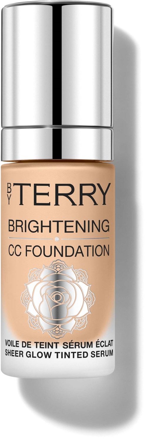 En beige flaske med sølvhette, merket 'By Terry Brightening CC Foundation' og dekorativt design.