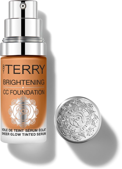 En flaske av BB Terry Brightening CC Foundation med en sølvpumpe og en rund sølbekopp ved siden av.