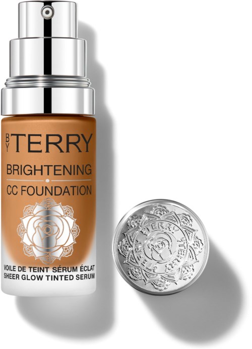 En flaske med BB Terry Brightening CC Foundation og en sølvet kompakt med blomsterdekorasjon.