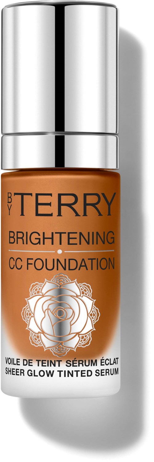 Liten flaske med sølvtopper, oransje kropp og blomsterdesign. Den er merket "BY TERRY Brightening CC Foundation."
