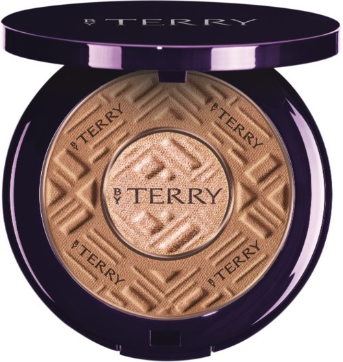 A compact with a patterned beige powder inside, labeled 'BY TERRY,' has a purple lid with the brand name.