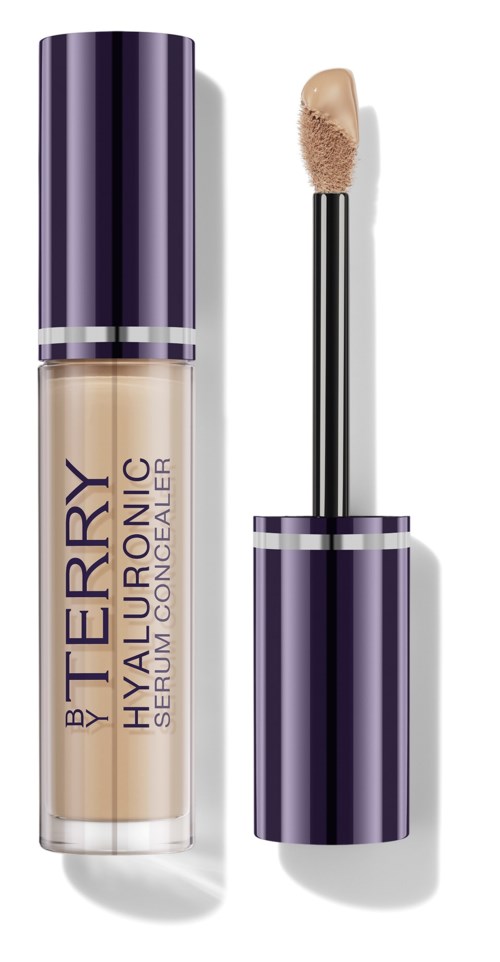 A concealer bottle with a purple cap, labeled 'by Terry Hyaluronic Serum Concealer,' with applicator beside it.