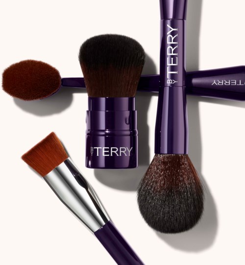 Four makeup brushes with purple handles and different sized bristles are arranged on a white background.