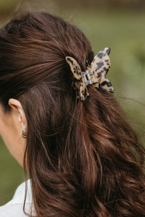 A woman with long, brown hair wears a butterfly-shaped hair clip outdoors.