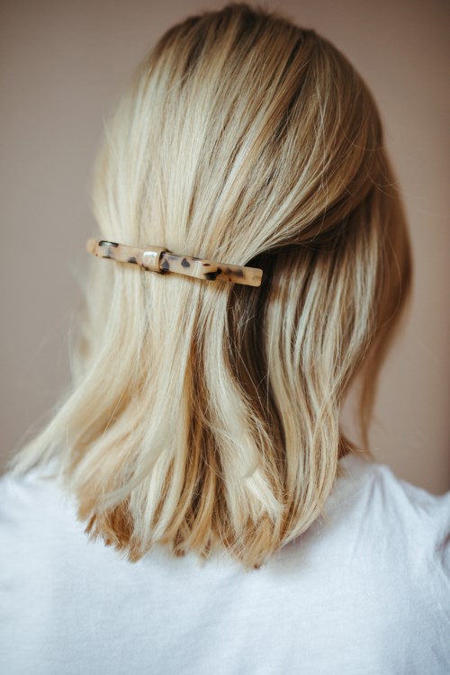 En kvinne med blondt hår som er festet bak med en liten, beige og brun hårklemme, iført en hvit topp.