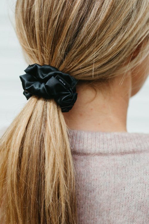 En flicka med blont hår i hästsvans med en svart scrunchie, bär en ljusrosa tröja.