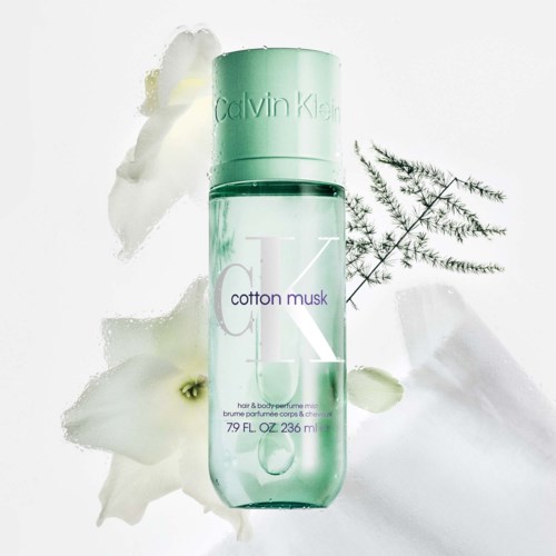 En flaska Calvin Klein Cotton Musk-parfym med vita blommor och gröna blad runt den.