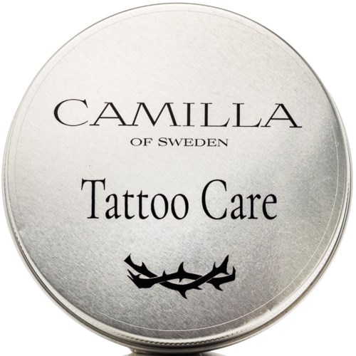 Ett runt silverfärgat lock med texten 'Camilla of Sweden Tattoo Care' och ett svart dekorativt streck under.