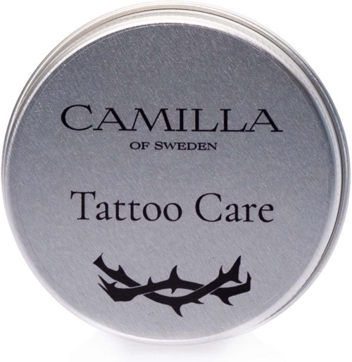 En rund silvrig etikett på en behållare med texten 'Camilla of Sweden Tattoo Care' och en svart taggig gren.
