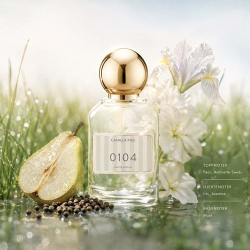 En parfymeflaske merket Camilla Piu med duftnoter av pære, jasmin og musk, omgitt av pære og blomster på en grønn overflate.