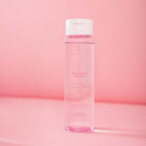 En lång, tydlig rosa flaska märkt 'Moisture Boost Micellar Cleansing Water' mot en rosa bakgrund.