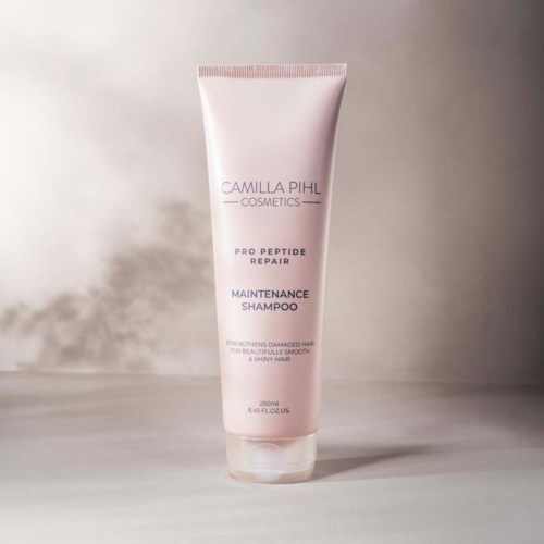 A pink tube of Camilla Pihl Cosmetics shampoo with white and purple text, standing on a flat surface.