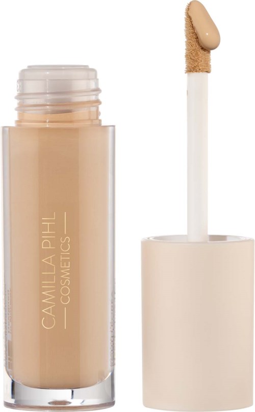 Beżowy płynny podkład z białą nakładką i aplikatorem. Butelka ma nazwę 'Camilla Pihl Cosmetics'.