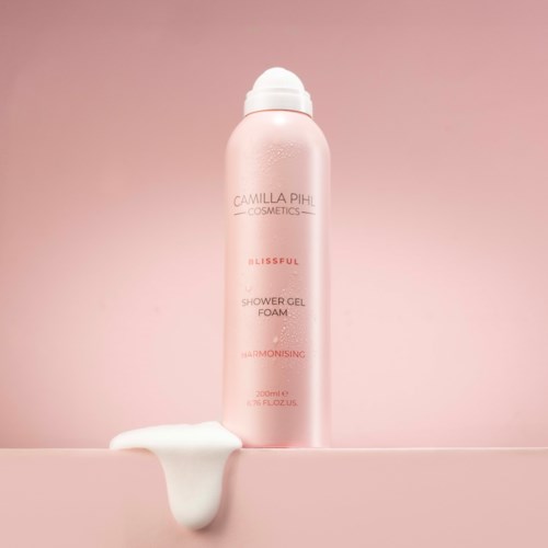 Lyserosa dusjgelflaske med lotion som renner ut ved siden av på en rosa bakgrunn.