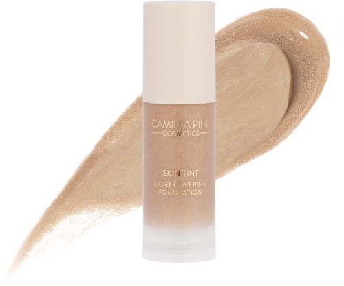 En foundationflaska märkt 'Camilla Pihl Cosmetics Skin Tint' med en beige svansbakgrund.