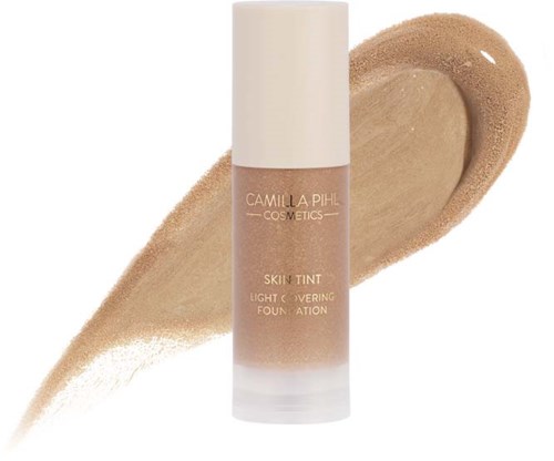 En foundationflaska i beige färg med etikett som säger 'Camilla Pihl Cosmetics Skin Tint Light Covering Foundation' och en provs högst bak.