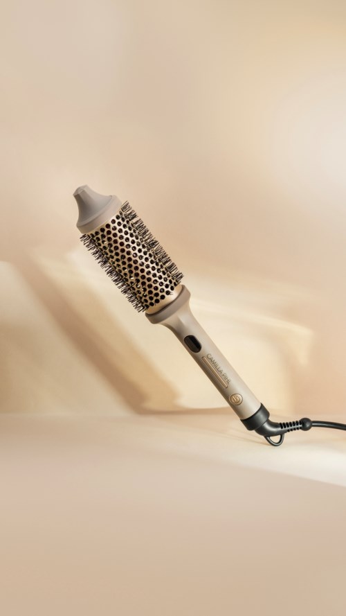Een stylingtool met ronde borstel, aangesloten, leunend tegen de muur.