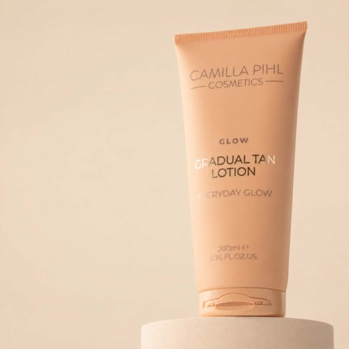 A peach-colored tube of Camilla Pihl Cosmetics glow lotion standing on a white surface.