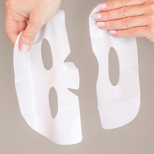 Twee handen houden stukjes van een gezichtsmasker met uitsparingen, mogelijk voor huidverzorging of cosmetica.