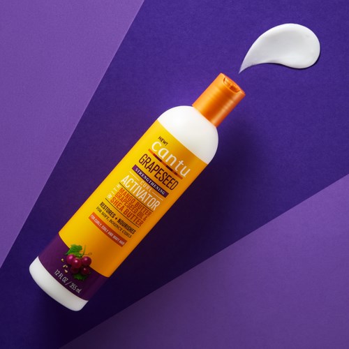 A bottle of Cantu Grapeseed Activator with a small amount of cream on the purple background.