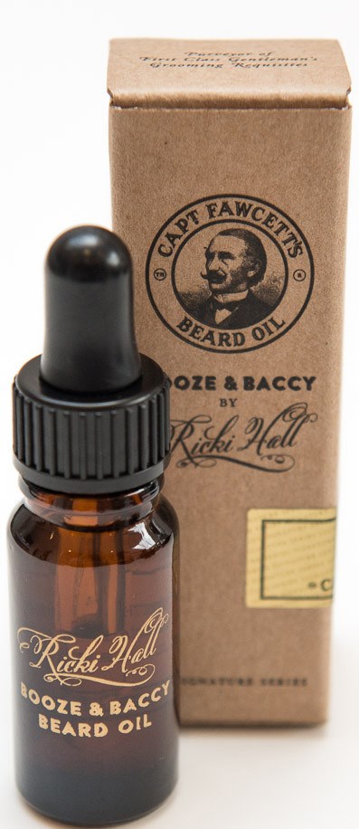 En lille brun flaske med dropper låg ved siden af en beige kasse, begge mærket 'Ricki Hall Booze & Baccy Beard Oil.'