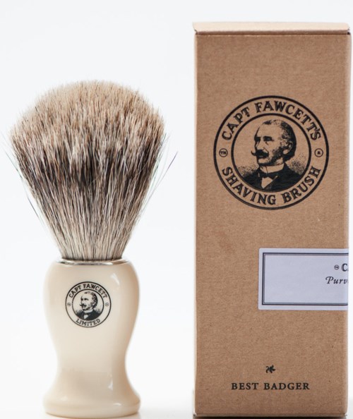 En rakborste med beige handtag och borst, bredvid en brun förpackning med logga och text.
