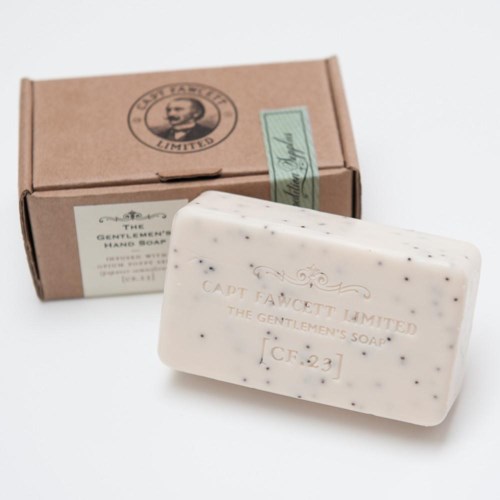 En vit tvålkaka med svarta prickar och en brun låda med texten 'The Gentlemen's Soap' samt en logga med ett mansansikte.