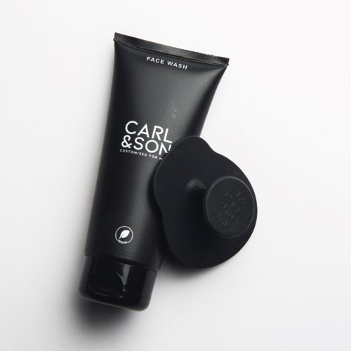 Een zwarte tube gezichtsreiniger met het label Carl & Son en een zwarte gezichtsborstel.