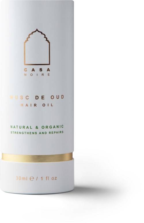 En vit flaska märkt 'CASA NOIRE' innehåller doftande oud-hårolja, med betoning på naturliga och organiska ingredienser, med guld- och gröna detaljer.