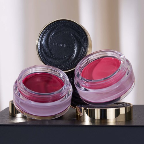 Twee open roze lipbalsems of crèmes in glazen potjes met zilveren voetjes, geplaatst op een zwarte ondergrond.