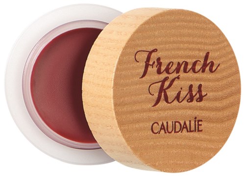 En liten rund behållare med röd läppbalsam och ett trälock med texten "French Kiss" av Caudalie.