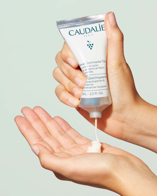 En person använder en tub med kräm från Caudalie för att gör huden mjuk, mot en ljus bakgrund.