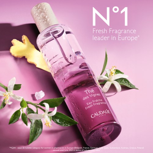 En rosa parfymflaska med blommor och ingefära på en rosa bakgrund, reklam för Caudalie, ett franskt doftmärke.
