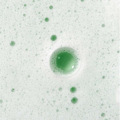 En grön vätska bubblar i ett vitt skum, med många små och några stora bubblor som svävar runt.