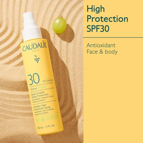 En gul solkrämflaska med SPF 30, märkt för ansikte och kropp, placerad på sand med ett grönt druvor nära.