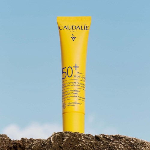 En gul solkrämstub med SPF 50+ står på en sten, med en blå himmel och hav i bakgrunden.