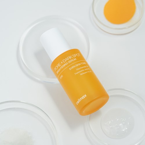 Orangene Flasche mit Pore + Dark Spot, Anti-Unreinheiten-Serum, auf weißer Oberfläche mit kleinen Schalen.