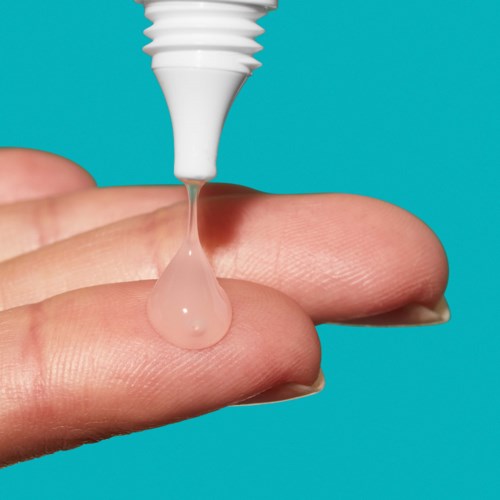 En liten droppe klart vätska är på att falla från en vit tub på ett finger.