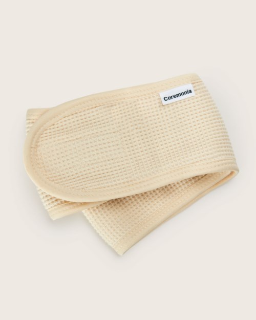 A beige elastic band labeled 'Ceremonia' with a textured surface. It is folded and looks soft and stretchy.